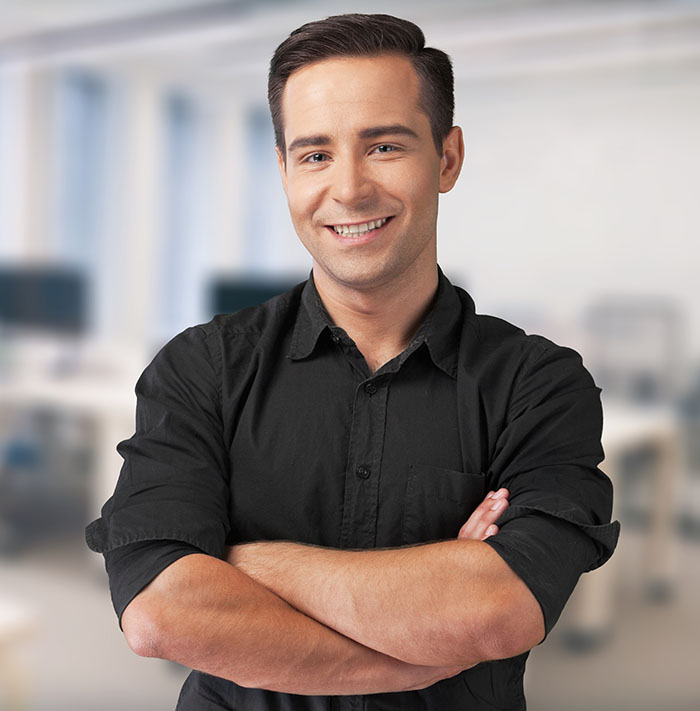 Smiling confident young businessman standing with folded hands